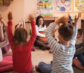Smiling female teacher playing a guitar during music class in a preschool.