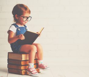 happy child little girl with glasses reading a books